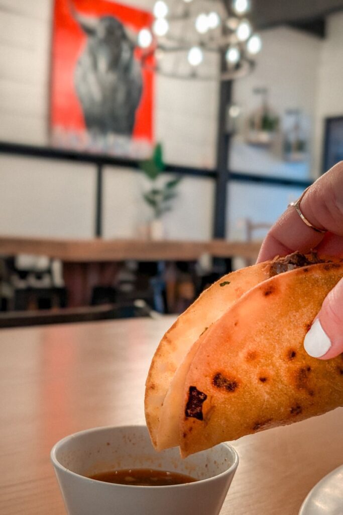 a hand holding and dipping a birria taco at moms tacos