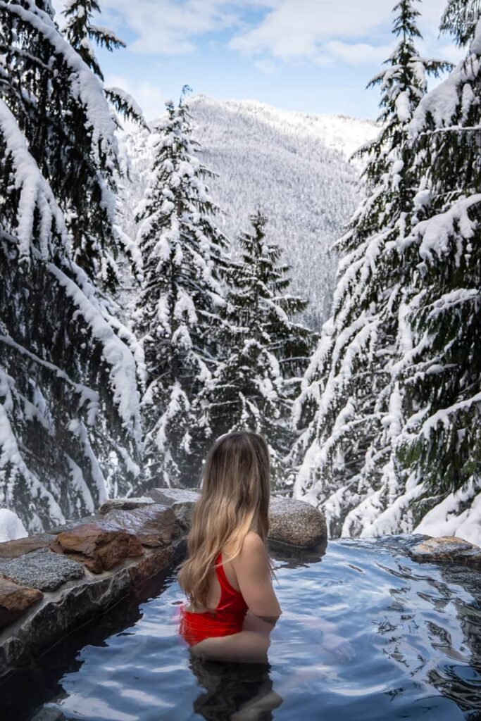 women in red swimsuit soaking at scenic hot springs surrounded by snowy landscape